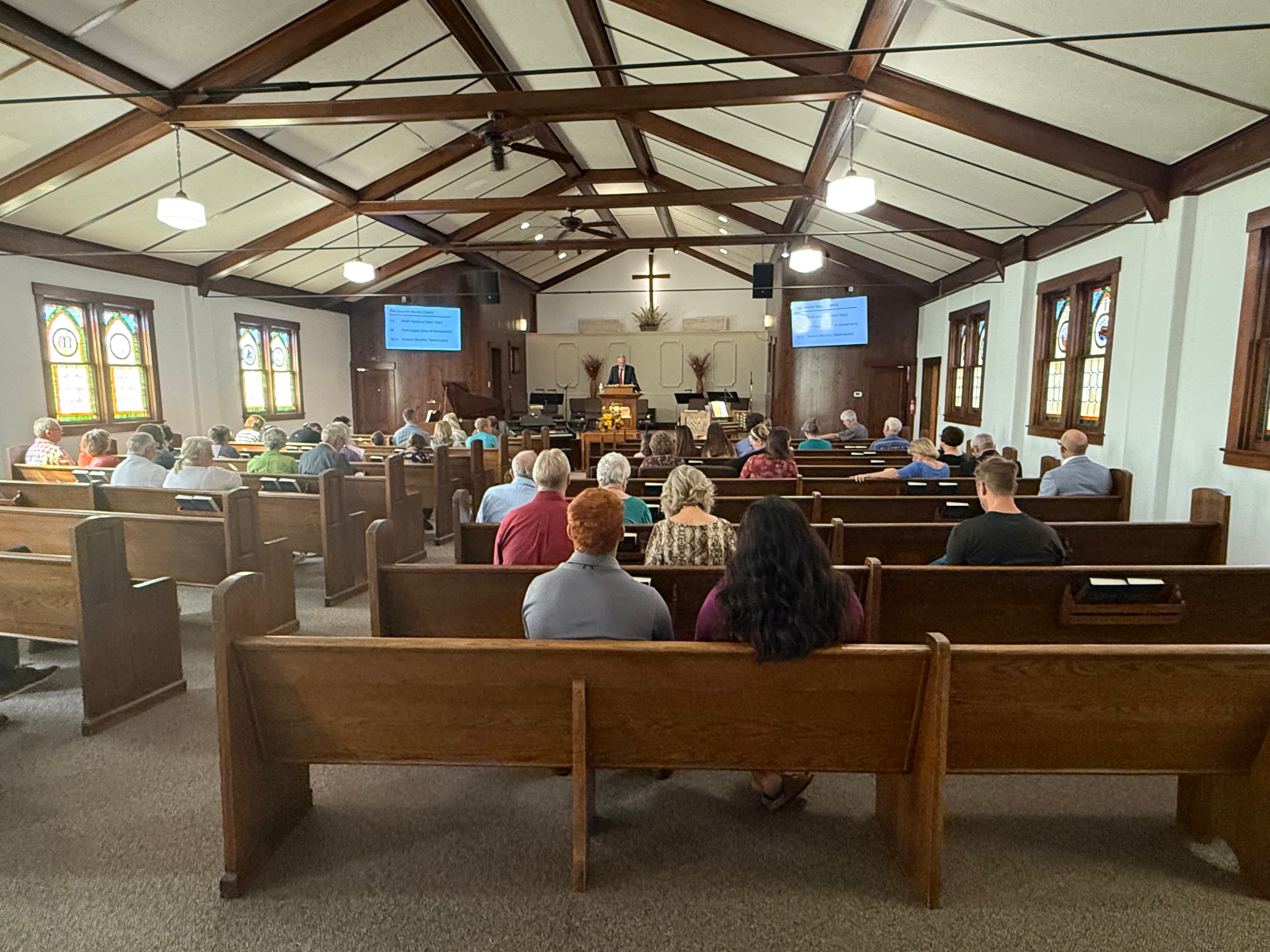 The congregation of Trinity Evangelical Church gathered in the sanctuary for Lord's Day worship, facing the pulpit beneath the wooden cross and open-beam ceiling.