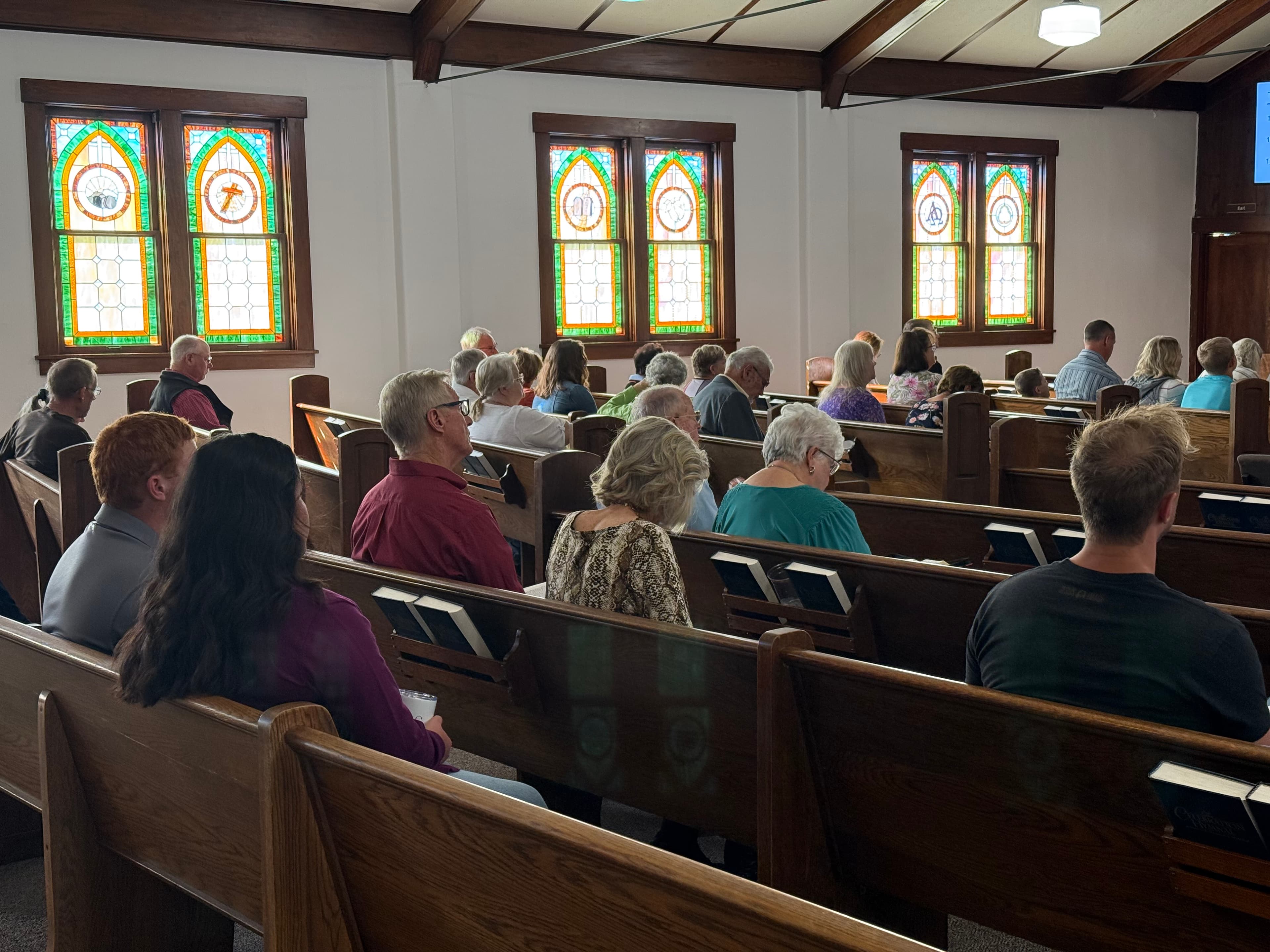 Members of the congregation seated in the oak pews on a Sunday morning, with the sanctuary's arched stained-glass windows along the wall behind them.