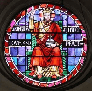 A stained-glass window at Trinity Evangelical Church depicting Christ enthroned in majesty, ringed with the inscription 'A Kingdom of Justice, Love and Peace'.